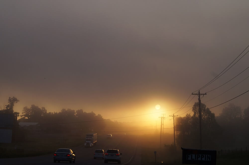 Highway leading into Flippin towards a foggy morning sunrise.